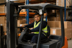 Un cariste professionnel portant un gilet haute visibilité conduit un chariot élévateur dans un entrepôt de stockage.
