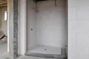 Receveur de douche blanc installé dans une niche en parpaings bruts, avec un espace vide visible sous le receveur.