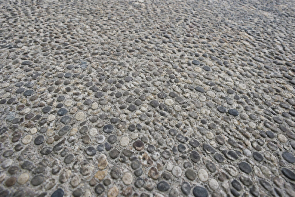 Texture en gros plan d'un revêtement de sol en béton désactivé composé de petits graviers arrondis.