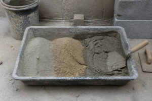 Bac de chantier contenant du ciment, du sable et du mortier préparé avec une truelle sur un sol en béton.