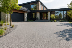 Allée de garage en béton drainant texturé devant une maison contemporaine avec bardage en bois et pierre.